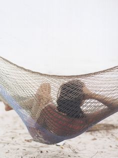 a man laying in a hammock on the beach with his back to the camera