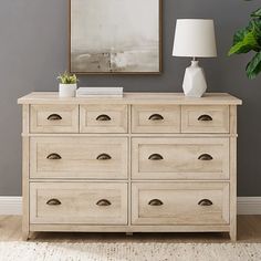 a large white dresser with drawers and a lamp on top of it in front of a gray wall