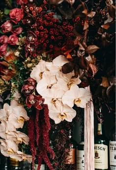 an arrangement of flowers and wine bottles on a shelf in front of a floral wall