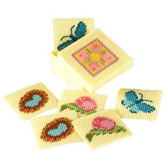 four coasters with cross stitch designs on them, one is blue and the other has pink flowers