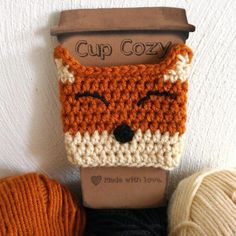 an orange and white crocheted fox head on top of a cup holder next to balls of yarn