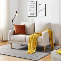 a living room with a white couch and yellow throw blanket on the floor next to it