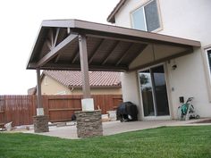 a covered patio with a bike parked on the grass in front of it and a house