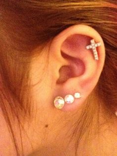 a close up of a person's ear with two piercings on it and a cross in the middle