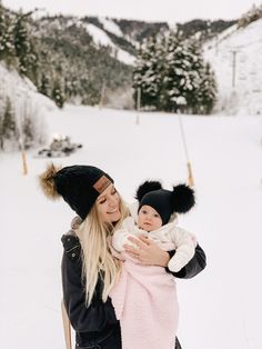 a woman holding a baby in her arms while wearing a black hat and pink blanket