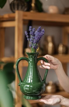 a person holding a green vase with purple flowers in it