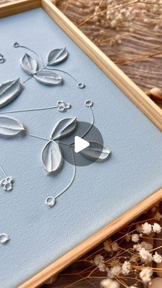 an embroidery project is displayed on a wooden surface with dried flowers in the foreground