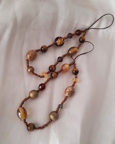 🦋 This smartphone chain features gemstones in sandy and brown tones, creating an earthy and natural look. The beads are recycled vintage pieces, and there are bronze citrine, wood and glass pearl elements in a warm orange hue.  Stretchable, sturdy, and reliable cord. The chain is stretchable, making it versatile for use as a keychain as well. Suitable for both iPhones and Android phone cases. Please note that each chain varies slightly, as they are made from natural gemstones and recycled vinta Bohemian Brown Beads With Gold Details, Spiritual Brown Beaded Chain Necklaces, Bohemian Brown Beaded Chain, Adjustable Brown Beaded Necklace With Gold Beads, Adjustable Brown Beaded Necklaces With Gold Beads, Brown Wooden Beads For Jewelry Making, Adjustable Brown Beaded Necklace With Gemstone Beads, Brown Beaded Healing Jewelry, Copper Jewelry With Colorful Beads