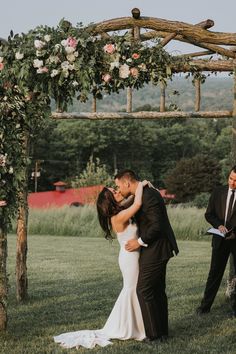 a bride and groom sharing a kiss under an arch with flowers on it at the end of their wedding ceremony