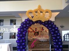 an entrance to a banquet hall decorated with purple balloons and a gold crown on top