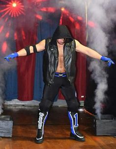 a man in black jacket and blue gloves standing on stage