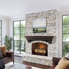 a living room filled with furniture and a fire place in front of two windows that look out onto a field