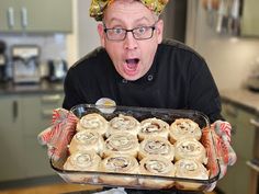 a man holding a pan full of rolls in his hands and making a surprised face