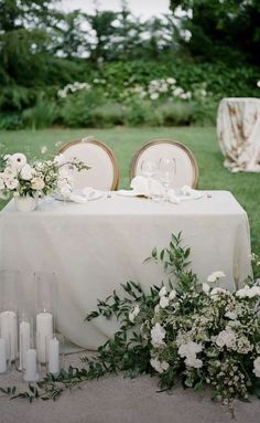 the table is set with white flowers and candles for an elegant wedding reception in the garden