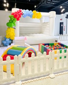 an indoor play area with white fence and rainbow colored balls in the air, on display at children's birthday party