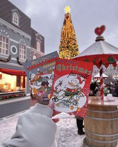 a person holding up two books in front of a christmas tree