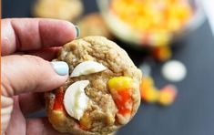 a hand holding a cookie with candy corn on it and some other food in the background