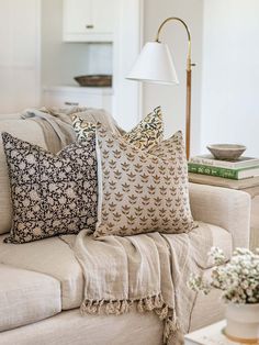 pillows on a couch in a living room with a lamp and vase full of flowers