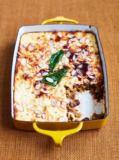 a casserole dish with meat and vegetables in it on a brown tablecloth