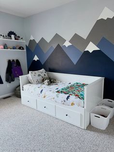 a child's bedroom with mountains painted on the wall and white drawers underneath it