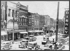 an old black and white photo of cars driving down the street