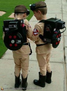 two young boys dressed in costumes standing next to each other on the sidewalk with electronic gadgets attached to their backs