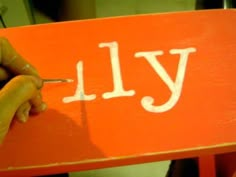 someone is writing the word july on an orange sign with white lettering and a pencil