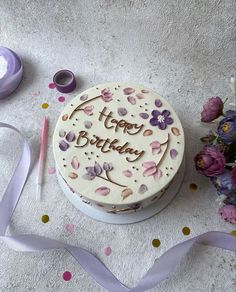 a birthday cake with purple flowers and ribbon on the table next to it is decorated