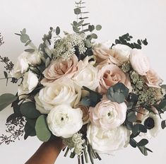 a hand holding a bouquet of white and pink flowers with greenery on the stems