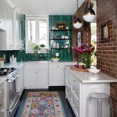 a kitchen with white cabinets and green tile backsplash, an area rug on the floor