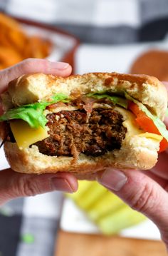 a hand holding a sandwich with meat, cheese and lettuce in it's bun