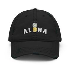 A tropical blend of laid-back style and island vibes, perfect for those who carry a bit of paradise wherever they go! Crafted from durable, distressed black fabric, this cap exudes effortless cool with a touch of beachy charm. The front of the cap features the cheerful phrase "Aloha" embroidered in vibrant colors, accompanied by a cute pineapple, symbolizing hospitality and tropical fun. It's a whimsical nod to the spirit of Hawaii, bringing sunshine and smiles no matter where you are. With its classic baseball cap design, distressed fabric, and adjustable strap, this cap offers a comfortable and customizable fit for island dreamers of all ages. Whether you're lounging by the pool, exploring the city, or daydreaming of sandy shores, this cap is your perfect companion for adding a splash of Cotton Baseball Cap For Beach, Black Dad Hat For Beach, Casual Cotton Trucker Hat For Vacation, Casual Baseball Cap For Beach Season Vacation, Distressed Curved Brim Hat For Beach, Trendy Black Baseball Cap For Vacation, Distressed Curved Brim Hats For The Beach, Black Baseball Cap For Vacation, Casual Black Dad Hat For Beach