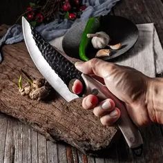 a person holding a knife on top of a wooden table next to mushrooms and other items