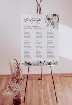 a wedding seating chart with flowers and greenery on it in front of a white wall