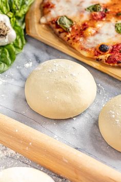 three uncooked pizza doughs sitting on top of a table next to vegetables