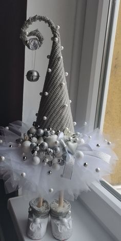 a christmas tree made out of white and silver balls on a window sill with baby shoes