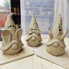 three clay sculptures of gnomes with hats and glasses on top of a table in front of a window