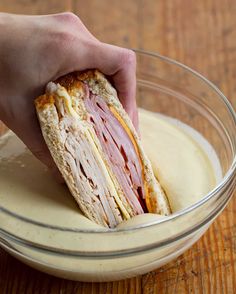 a ham and cheese sandwich is being held in a glass bowl on a wooden table