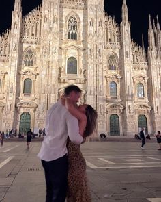 a man and woman standing in front of a large building with tall towers at night