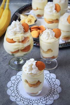 small desserts with bananas and whipped cream in glass dishes on a doily next to other desserts