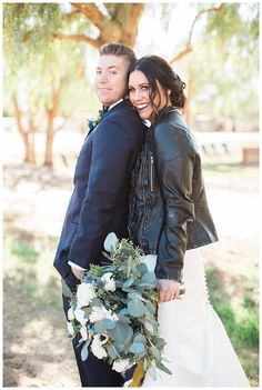 a bride and groom pose for their wedding photo in front of a tree with greenery