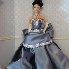 a barbie doll wearing a blue dress and white gloves sitting on top of a bed