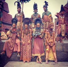 a group of people standing next to each other in front of a stone wall with statues on it