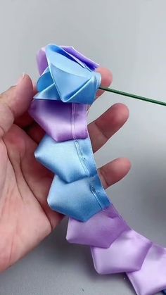 a person is holding a flower that has been folded in purple and blue ribbons on it