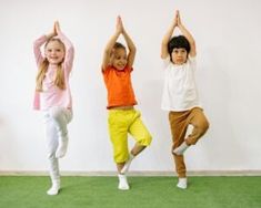 three children doing yoga poses in front of a white wall and green carpeted floor