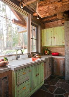 a kitchen with green cabinets and stone flooring in front of a window that looks out onto the woods