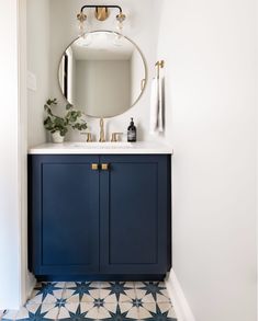 a bathroom with blue cabinets and a round mirror on the wall above it is tiled flooring