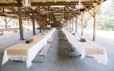 tables and benches are lined up in an old covered area with chandeliers hanging from the ceiling