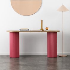 a pink table sitting in front of a white wall with a circular mirror on it