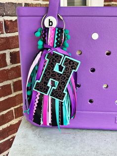 a purple purse with the letter e on it and a tassel hanging from it